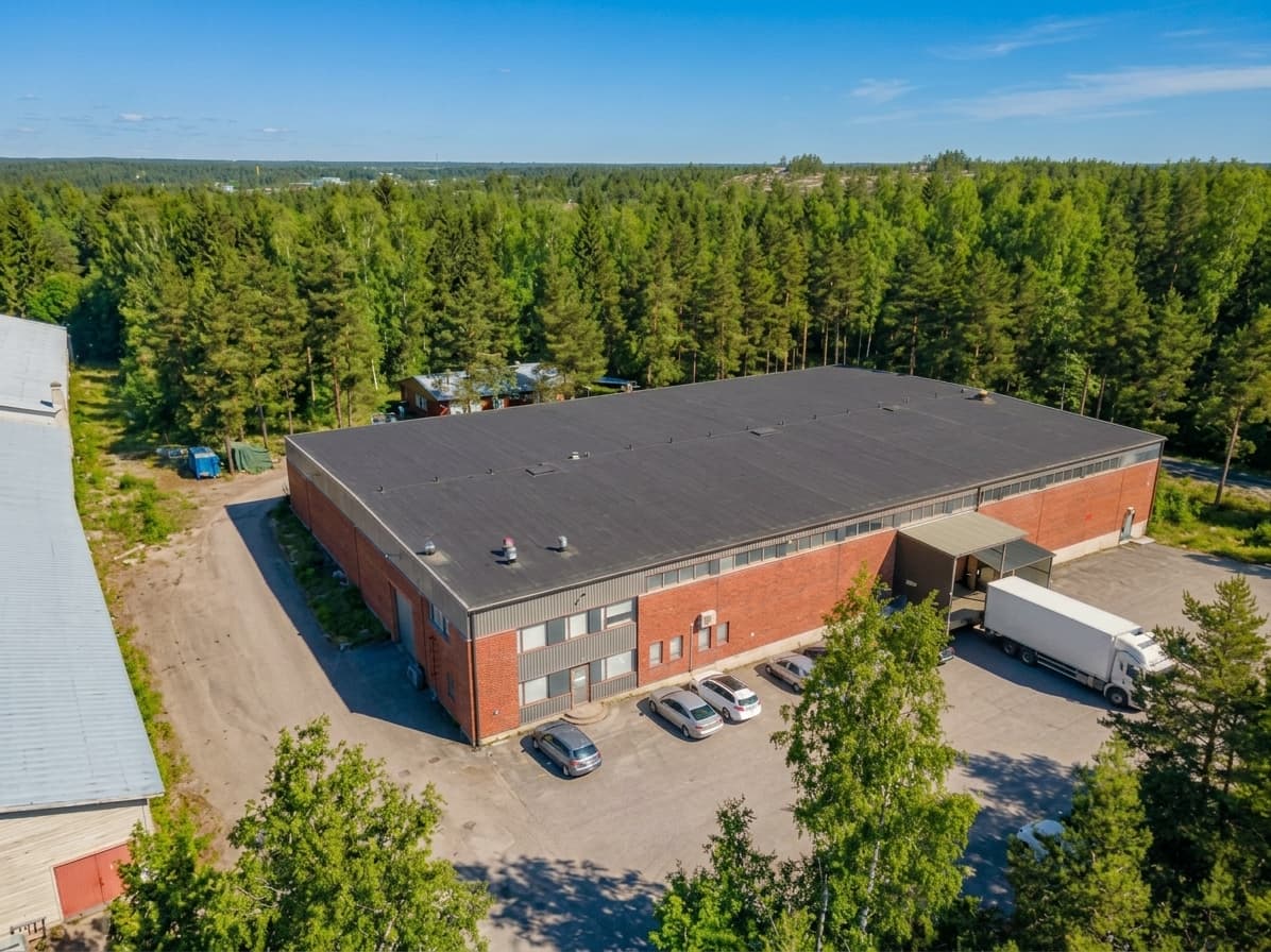 JL Levytekniikan tuotantolaitos ilmasta kesällä: punatiilinen tuotantohalli, toimistosiipi ja lastauslaituri metsän keskellä